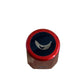 A close-up top-down view of a small cylindrical product with a metallic red rim, a dark navy blue center, and a white curved logo, placed on a beige textured surface.